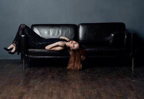skön kvinna med ljus smink lögner på en läder soffa närbild röd hår modell foto