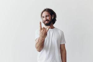 eleganta man i en vit t-shirt med trådlös hörlurar i hans öron har roligt lyssnande till musik leende på en vit bakgrund livsstil foto