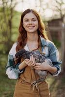 en Lycklig ung kvinna leende och innehav en ung kyckling den där lägger ägg för henne bruka foto