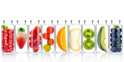 hemlagad hudvård med fruktingredienser av avokado, apelsin, blåbär, granatäpple, jordgubbe och hallon i glasflaskor isolerad på vit bakgrund foto