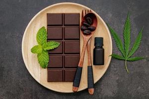 cannabisblad med mörk choklad, växtblad och träredskap på en mörk betongbakgrund foto