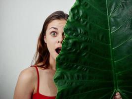 glad emotionell kvinna stor grön blad omslag henne ansikte röd baddräkt foto