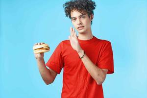 kille med lockigt hår i röd t-shirt hamburgare snabb mat blå bakgrund foto