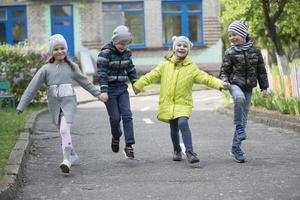 Lycklig förskolebarn på de gata. barn innehav händer Hoppar. en grupp av sex år gammal vänner. foto