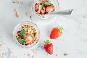 summet gott frukost. burkar med parfaits tillverkad av granola, jordgubbar, yoghurt på marmor tabell foto