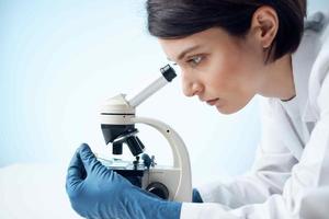 kvinna i vit täcka utseende genom mikroskop laboratorium vetenskap yrkesverksamma experimentera foto
