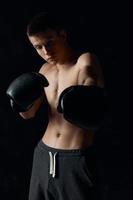 svart bakgrund manlig kroppsbyggare med en taggad torso i boxning handskar träna foto