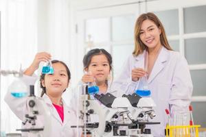 elementärt vetenskap klass, glad liten barn med lärare forskare som visar testa flaska med kemi flytande i skola laboratorium, vetenskap laboratorium foto