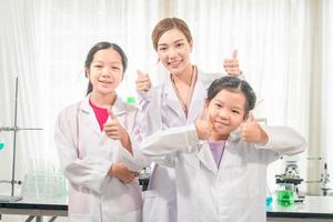 elementärt vetenskap klass, glad liten barn med lärare forskare som visar testa flaska med kemi flytande i skola laboratorium, vetenskap laboratorium foto