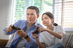 asiatisk far och dotter spelar video spel på Hem, människor håller på med aktiviteter och familj begrepp foto
