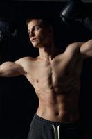 kille med en taggad torso gestikulerar med hans händer på en svart bakgrund boxning handskar kondition idrottare foto