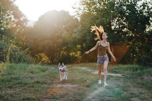 kvinna och henne hes hund lyckligt löpning genom de gräs i natur i de parkera leende med tänder falla promenad med sällskapsdjur, reser med en hund vän foto