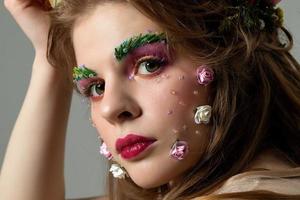 porträtt av en skön flicka med fantastisk sommar smink. vår flicka i blommor. de ansikte av en lyxig modell med utökad ögonbryn och ögonfransar. skönhet salong begrepp. foto