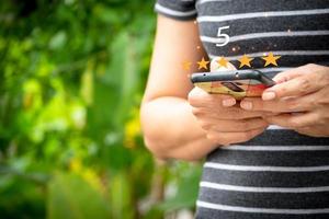 kvinna använder sig av smart telefon med 5 stjärna betyg på natur bakgrund, kund tillfredsställelse begrepp. kund service erfarenhet och företag tillfredsställelse undersökning. foto