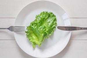 monotrofisk diet - två löv av sallad på de tallrik, gaffel och kniv, trä- bakgrund foto