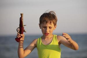 en pojke med en leksak pistol. en barn spelar en pirat på de bakgrund av de hav. foto