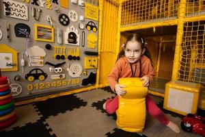 söt preschooler flicka spelar mot upptagen styrelse på barn spela Centrum. foto