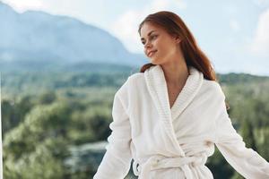 attraktiv ung kvinna lång hår i en vit morgonrock vistas på de balkong i en hotell berg se foto