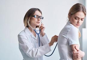 läkare i en medicinsk klänning med en stetoskop undersöker en patient på en ljus bakgrund foto