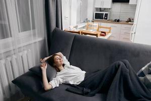 kvinna täckt med en filt är liggande på de soffa och ser upp de fönster i de bakgrund foto