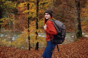 kvinna i höst parkera med fallen löv och ryggsäck på henne tillbaka flod i de bakgrund foto