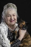 porträtt av en nittio år gammal kvinna med en sällskapsdjur. glad gammal lady med en katt. mormor på en svart bakgrund med en hårig djur. äldre skönhet. de gråhårig välvårdad pensionär. foto