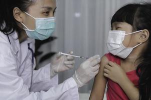 asiatisk läkare injektion vaccin för skyddande virus covid-19 till en flicka ha på sig medicinsk mask, människor är flickor är vaccinerade mot influensa varje år. foto