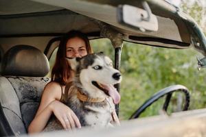 kvinna och henne hes hund lyckligt reser i bil leende med tänder höst promenad med sällskapsdjur, resa med hund vän foto