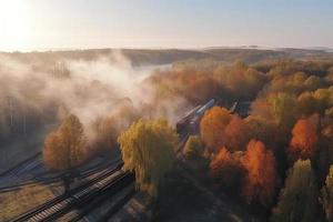 antenn se av frakt tåg i skön skog i dimma på soluppgång i höst. färgrik landskap med järnväg foto