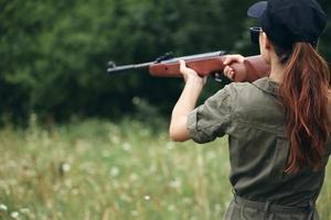 kvinna soldat innehav vapen i hand siktar jakt vapen grön träd foto