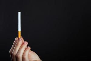 kvinnlig hand håller en cigarett på en mörk bakgrund foto