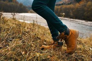 kvinnors fötter jeans skor torr gräs höst flod bergen i de distans foto