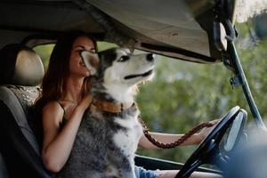 kvinna och henne hes hund lyckligt reser i bil leende med tänder höst promenad med sällskapsdjur, resa med hund vän foto