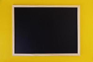 tom svart tavla på gul bakgrund. framifrån på svart tavla med träram. tomt kopiautrymme på platt panel. foto