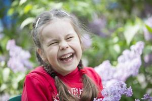 en barn i en lila. skrattande flicka preschooler med en bukett av vår blommor. foto