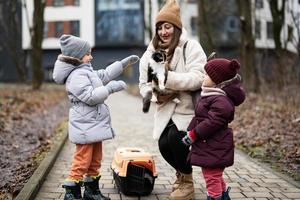 mor och döttrar med katt i resa plast bur transport utomhus- på parkera. foto