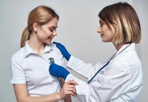 läkare kvinna med en stetoskop innehar en patient förbi de axel på en ljus bakgrund foto