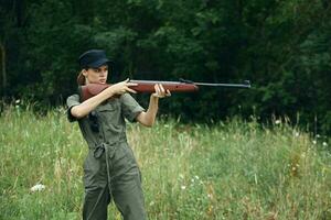 kvinna med en vapen i hand, en jakt grön overall är siktar färsk luft foto