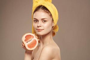 glad kvinna med gul handduk på henne huvud grapefrukt klar hud beige bakgrund foto