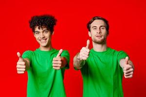 glad vänner i grön t-tröjor gestikulerar med händer känslor röd bakgrund foto