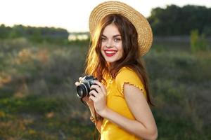 kvinna fotograf med en kamera i henne händer leende röd mun hatt gul t-shirt sommar natur foto