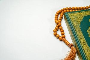 de helig al quran med skriven arabicum kalligrafi menande av al quran och radband pärlor eller tasbih på vit bakgrund med kopia Plats. foto