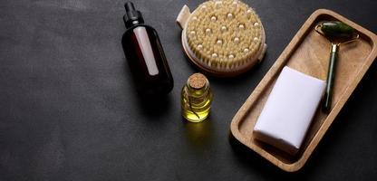 brun glas flaska för kosmetika, en bit av tvål insvept i papper och en borsta för torr kropp massage på en svart bakgrund foto