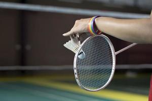 badminton spelare bär regnbåge armband och innehav racket och vit fjäderboll i främre av de netto innan tjänande den till spelare i annan sida av de domstol, begrepp för HBTQ människor aktiviteter. foto