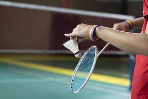 badminton spelare bär regnbåge armband och innehav racket och vit fjäderboll i främre av de netto innan tjänande den till spelare i annan sida av de domstol, begrepp för HBTQ människor aktiviteter. foto