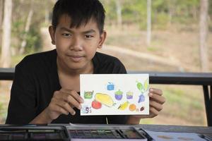 asiatisk pojke som visar hans vattenfärg teckning i händer. foto
