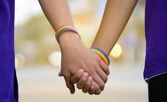 närbild händer som ha på sig regnbåge handledsband runt om dem av Gay par, begrepp för HBTQ människor presenter deras kärlek till Allt kön människor runt om de värld. foto