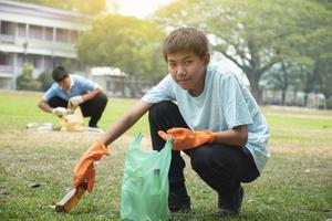ung asiatisk pojke sortering olika sopor och sätta dem in i de lådor framför av honom i de parkera, natur vård och miljö kärlek begrepp. foto