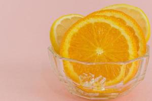 närbild av skivad färsk apelsin med isbitar på rosa bakgrund. foto