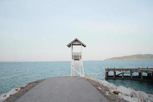 vit livräddare torn och gammal trä- bro med marinmålning se på de strand i thailand foto